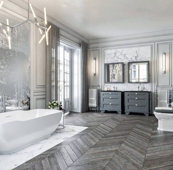 Luxurious bathroom with freestanding tub, marble accents, herringbone floors, and modern chandelier lighting.