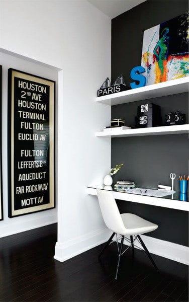 Modern home office with a white desk, chair, wall shelves, and subway sign decor, dark wood floor and gray accent wall