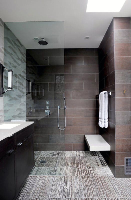 Contemporary shower with dark tiles, floating bench, patterned floor, and glass divider.