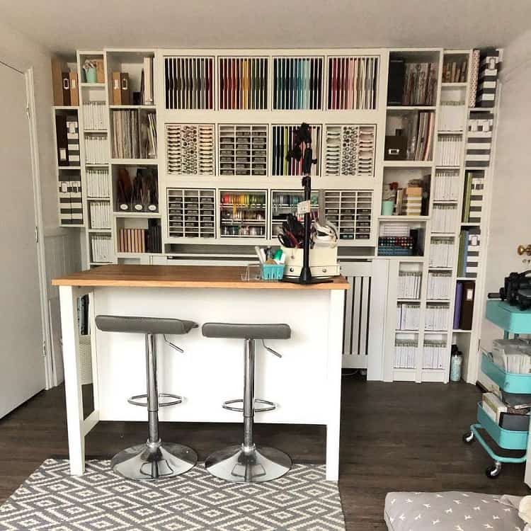 Craft room with organized shelves of materials, a white island table, and two stools on a gray patterned rug