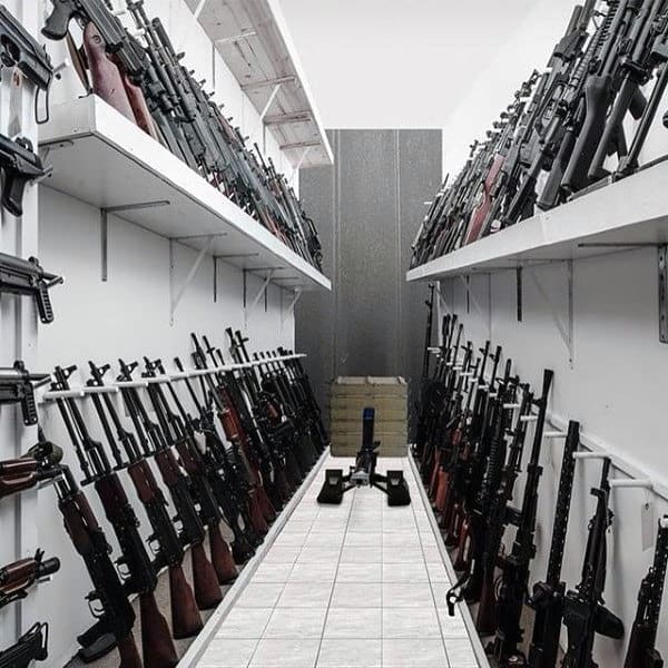Modern gun room with white walls, tiled floor, and rows of rifles on shelves and racks.