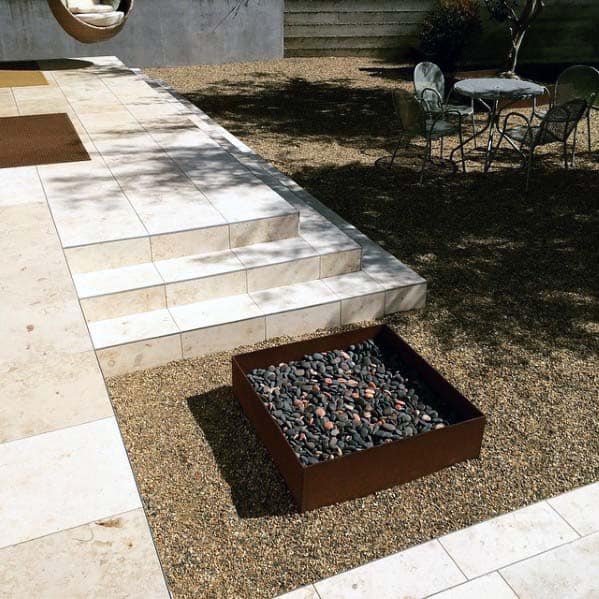 Modern patio with stone tiles, gravel, a square fire pit, and outdoor seating under a tree