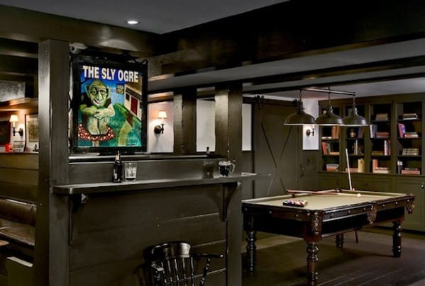 Cozy basement with pool table, bookshelves, a framed "The Sly Ogre" poster, and soft lighting