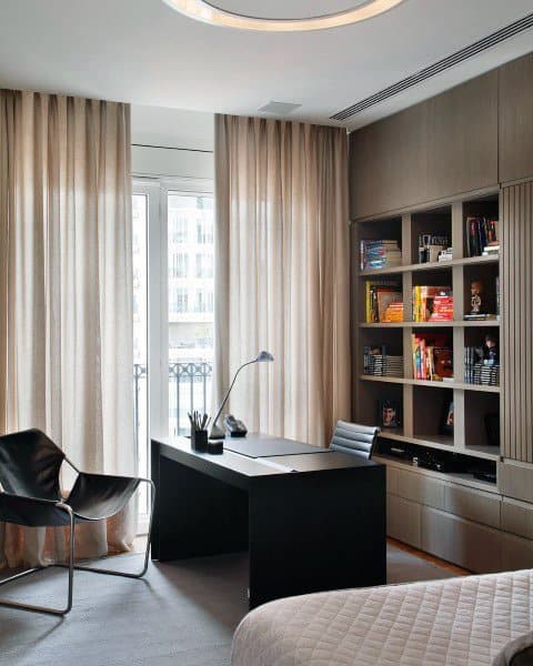 Modern home office with black desk, built-in shelves, and floor-to-ceiling curtains.