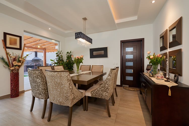 A modern dining room with a floating ceiling, elegant chandelier, tasteful decor, and large windows leading to an outdoor space, creating a refined and open atmosphere