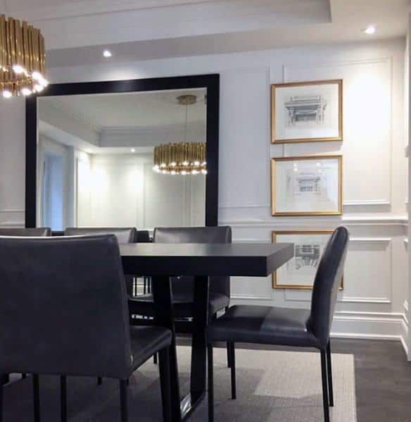 Modern dining room with a large mirror, chair rail, black table, dark chairs, and gold-framed artworks on the wall