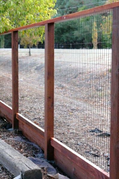 Gravel path and grassy area under a tree alongside a wooden fence with wire mesh
