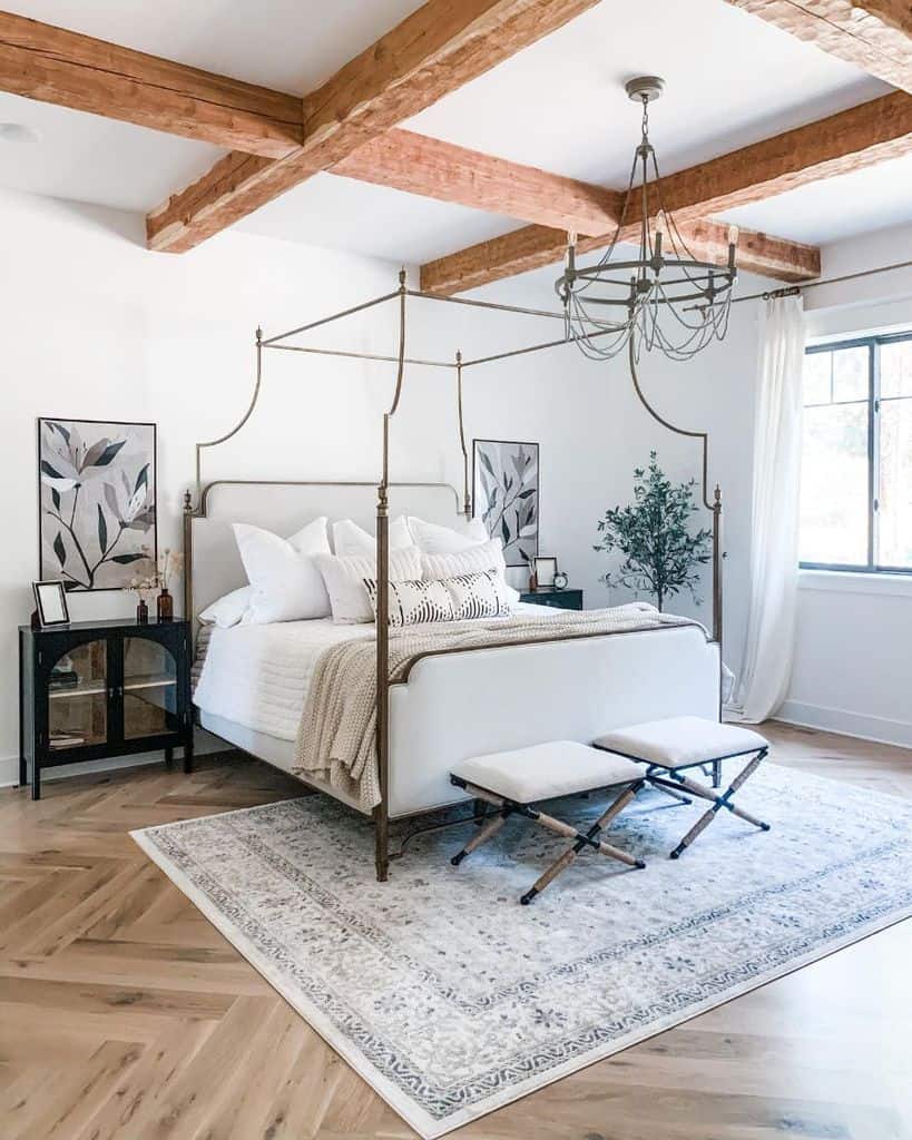 Farmhouse bright bedroom with a canopy bed, wooden beams, patterned rug, decorative plants, and a chandelier