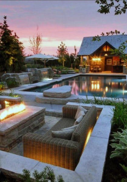 Cozy outdoor seating by a pool at sunset, with lights and a fire pit illuminating the lounge area and nearby building