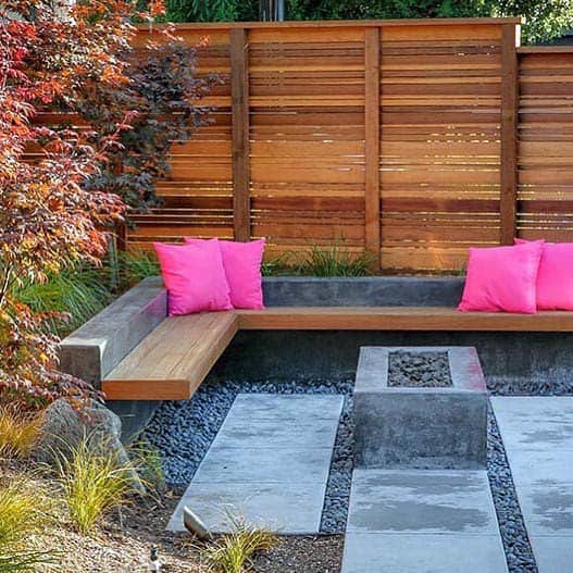 Modern outdoor patio with wooden seating, pink cushions, gravel pathway, and a wooden privacy screen