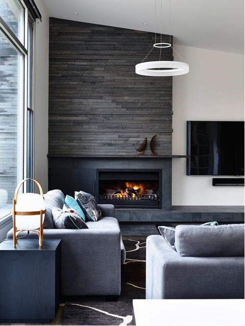 A contemporary living room with a sleek fireplace framed by dark textured tiles, complemented by gray furniture and modern decor elements.