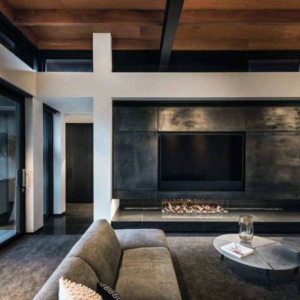 A stylish living room with a black-paneled fireplace and integrated TV, accented by wood ceiling beams and modern furniture.