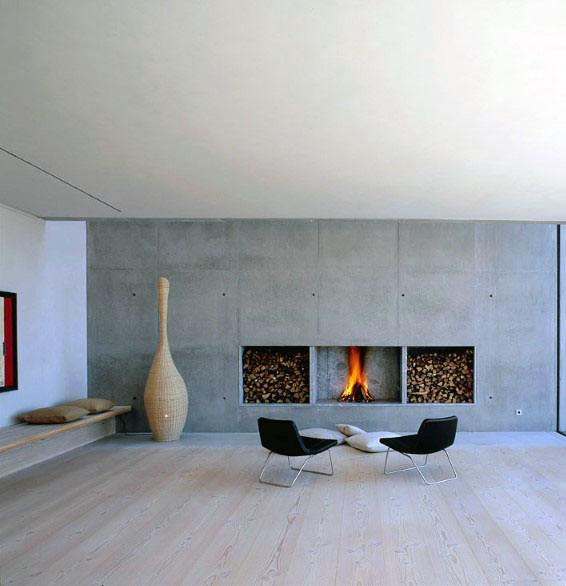 Modern fireplace with central fire, firewood storage, concrete wall, and minimalist decor.