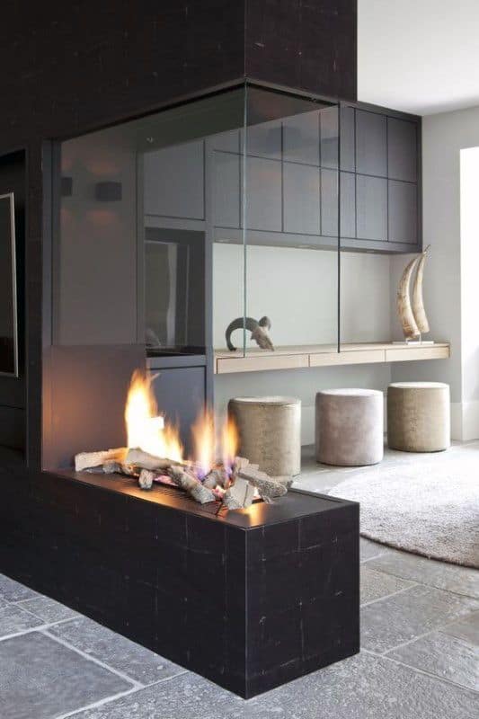 Contemporary glass-enclosed fireplace with black surround and cozy seating area.