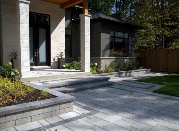 Modern front yard with paved walkway, tiered steps, minimal plants, and a wooden privacy fence.