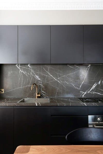 Sleek kitchen with black cabinets, dark marble backsplash, and brass faucet.