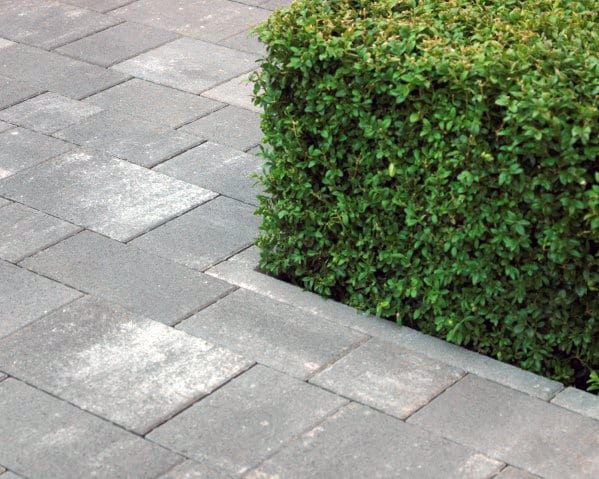Modern gray stone pavers with clean edging next to a neatly trimmed hedge.