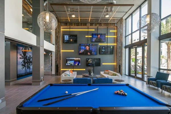 Modern lounge with a pool table, multiple TVs, and large windows; stylish seating and hanging lights enhance the space