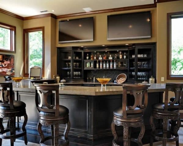 Home bar with high-backed chairs, two TVs, stocked shelves, and large windows for natural light—perfect bar setup