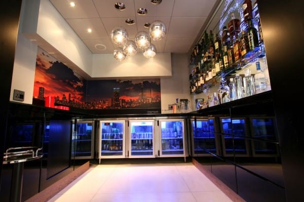 A modern bar with illuminated shelves, a cityscape mural, and glass orb lights hanging from the ceiling