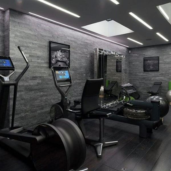Home-style modern gym with exercise machines, dark walls, and wooden floor; mirrors and framed photos on the walls