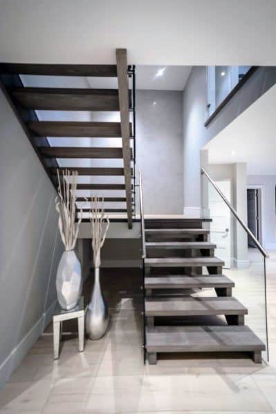 Modern floating stairs with dark wood steps and glass railing in a minimalist open-plan interior.