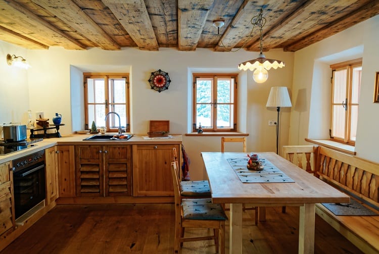A cozy kitchen with wooden ceiling beams, rustic cabinetry, and a dining table with seating, creating a warm, inviting atmosphere