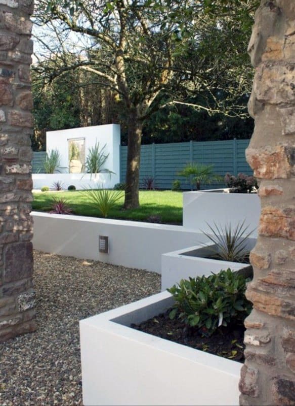 Modern garden with white raised planters, gravel pathway, and a central tree under soft lighting.