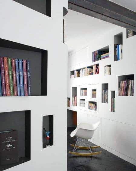 Modern white library with built-in shelves, vibrant books, and a cozy rocking chair on a dark floor