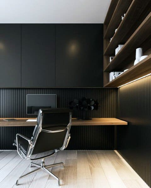 Minimalist home office with black walls, wooden desk, shelves, and sleek leather chair.
