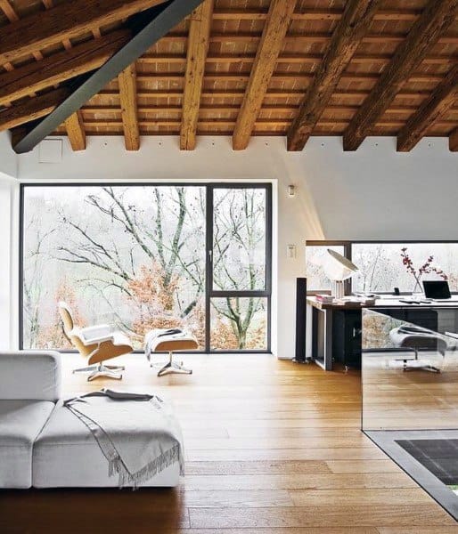 Rustic home office with wooden beams, large windows, and a cozy seating area.