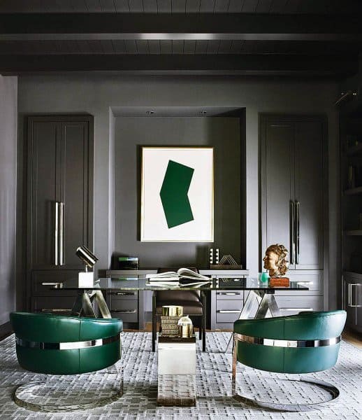 Modern home office with glass desk, green leather chairs, and sleek grey cabinets.