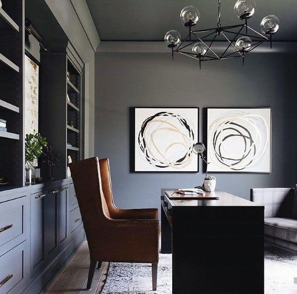 Modern home office with grey walls, abstract art, leather chair, and statement chandelier.