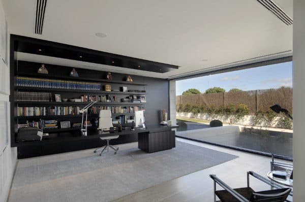 Spacious modern home office with wall-to-wall shelves, glass wall, and outdoor pool view.