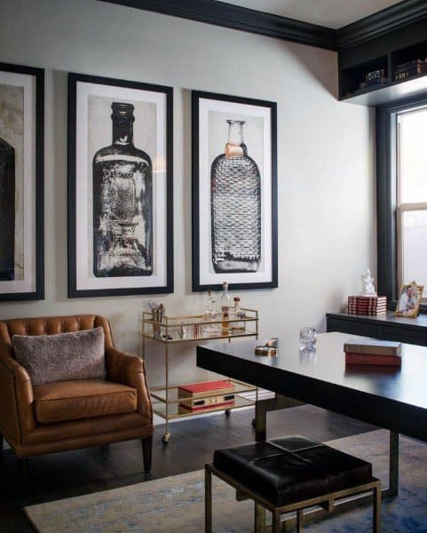 Sophisticated home office with leather armchair, bar cart, and framed artwork on the wall.
