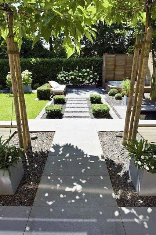 Modern backyard with stone pathways, manicured hedges, and shaded seating areas.