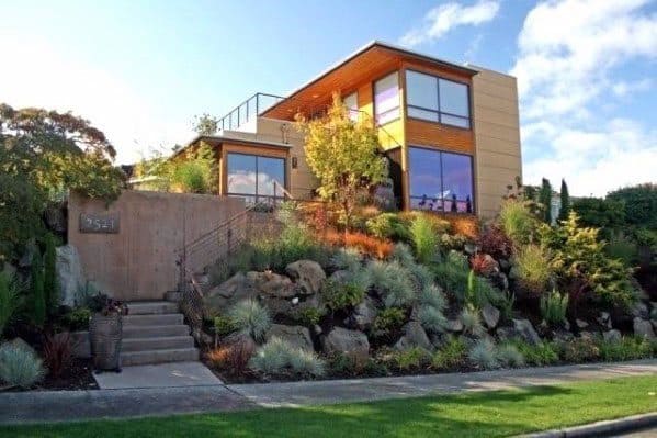 Modern front yard landscaping on a slope with large rocks, drought-tolerant plants, and a stylish contemporary house design