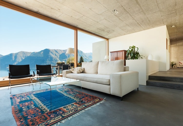 A modern living room with a textured concrete ceiling, minimalist furniture, and large windows offering stunning views of the mountains, creating a bright and open space