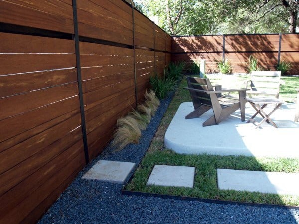 Modern horizontal wooden fence surrounding a cozy backyard patio with seating and landscaping.