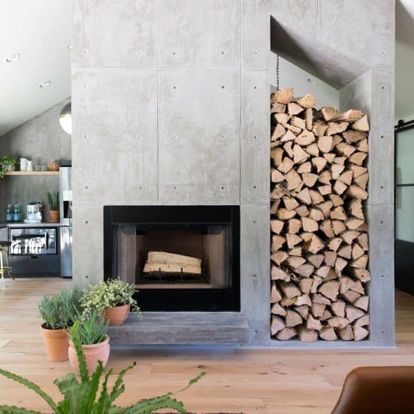 Concrete fireplace with integrated firewood storage and potted plants on a wooden floor.