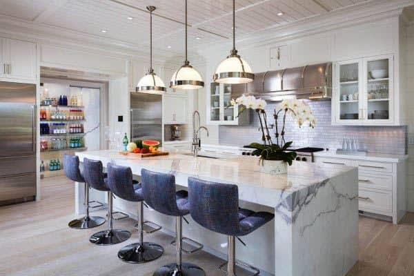 Bright kitchen with marble island, blue barstools, pendant lighting, and open pantry.