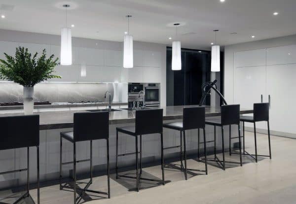 Sleek kitchen with white cabinets, black bar stools, pendant lighting, and a minimalist design.