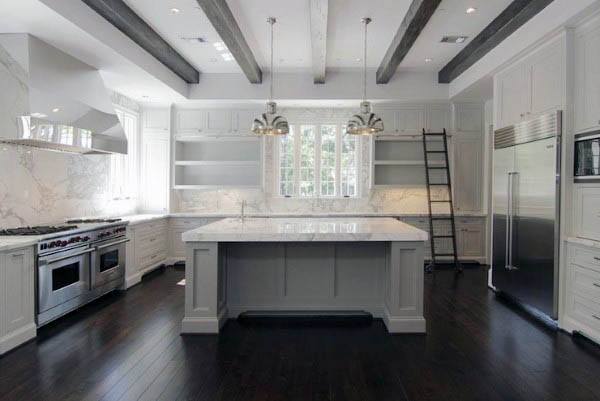 Bright kitchen with gray island, marble backsplash, exposed beams, and dark wood flooring.