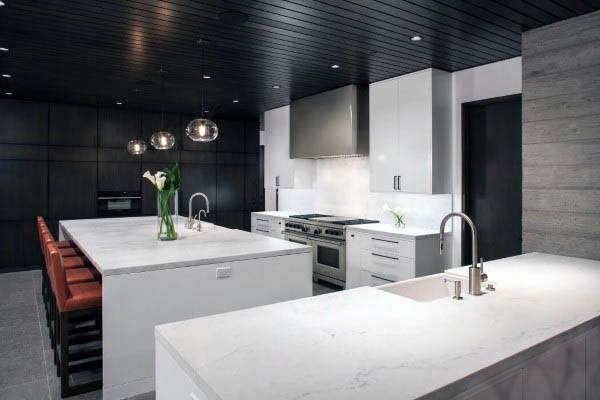 Modern kitchen with dual white islands, red barstools, black ceiling, and pendant lighting.