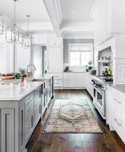 Bright kitchen with white cabinets, island, pendant lights, wooden floor, and a patterned rug