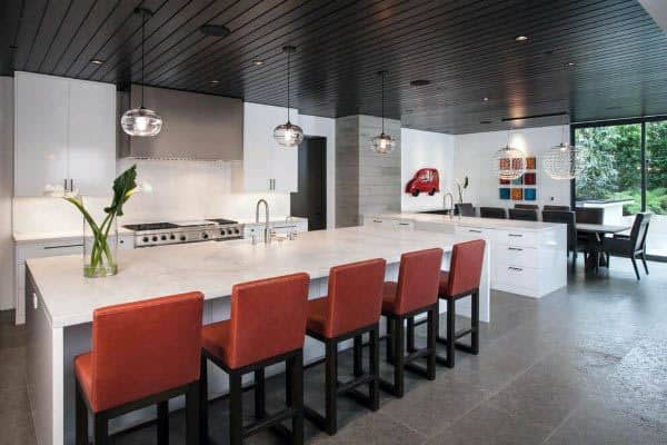 Contemporary kitchen with white island, red barstools, pendant lights, and black ceiling.
