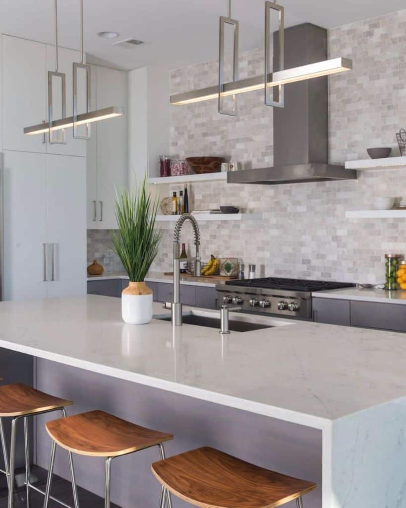 Modern kitchen with marble island wooden stools stainless steel hood and geometric pendant lights.