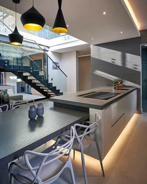 Modern kitchen with sleek island, unique pendant lighting, and a staircase backdrop.