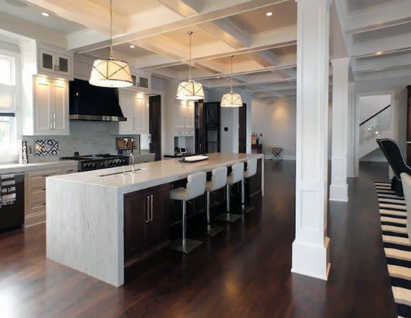 Spacious kitchen with marble island, coffered ceiling, dark wood floors, and pendant lighting.