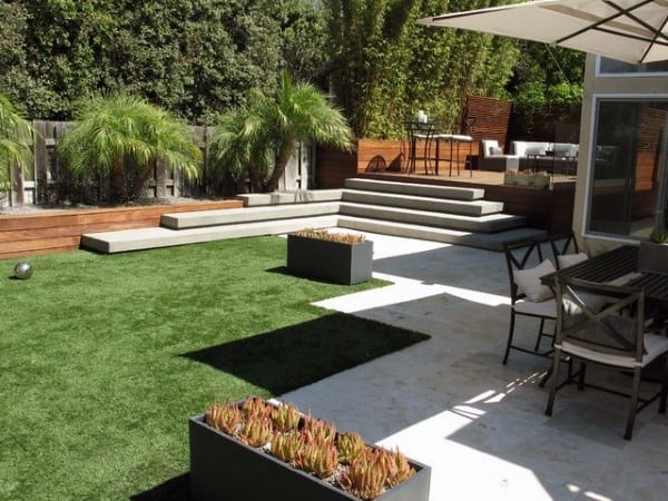 Modern backyard with artificial grass, raised planters, patio seating, and wooden accents.